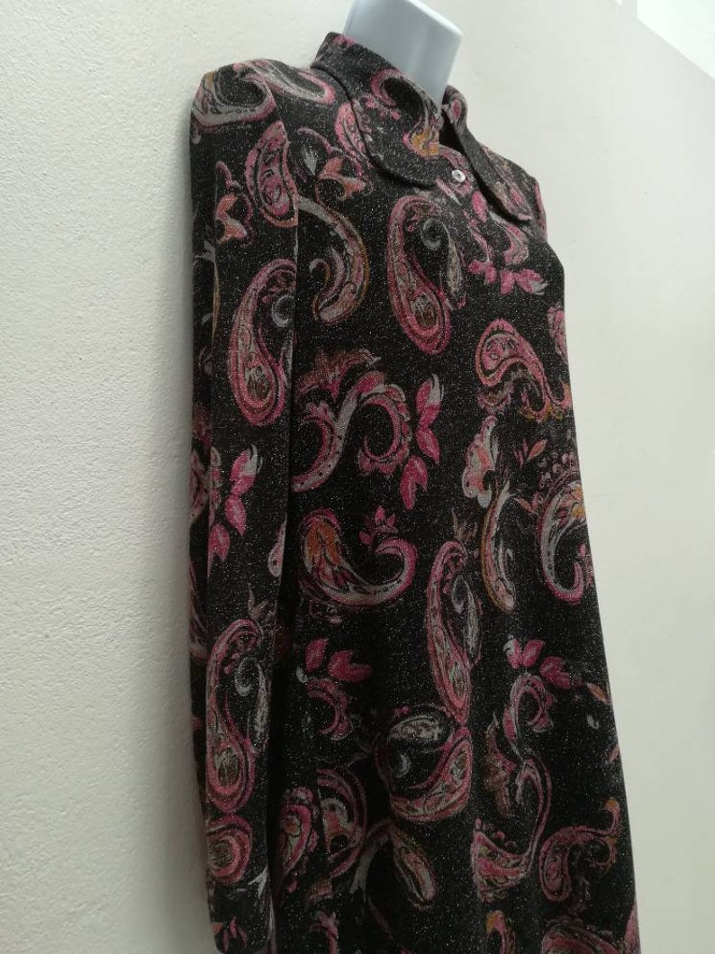 May include: A black long-sleeved dress with a paisley print in shades of pink, white, and brown. The dress has a collared neckline and a button closure.