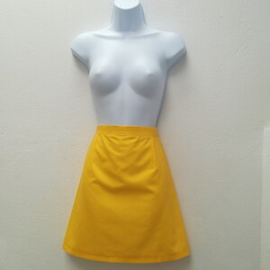 May include: A yellow mini skirt with a polka dot pattern. The skirt is made of a textured fabric and has a straight silhouette.