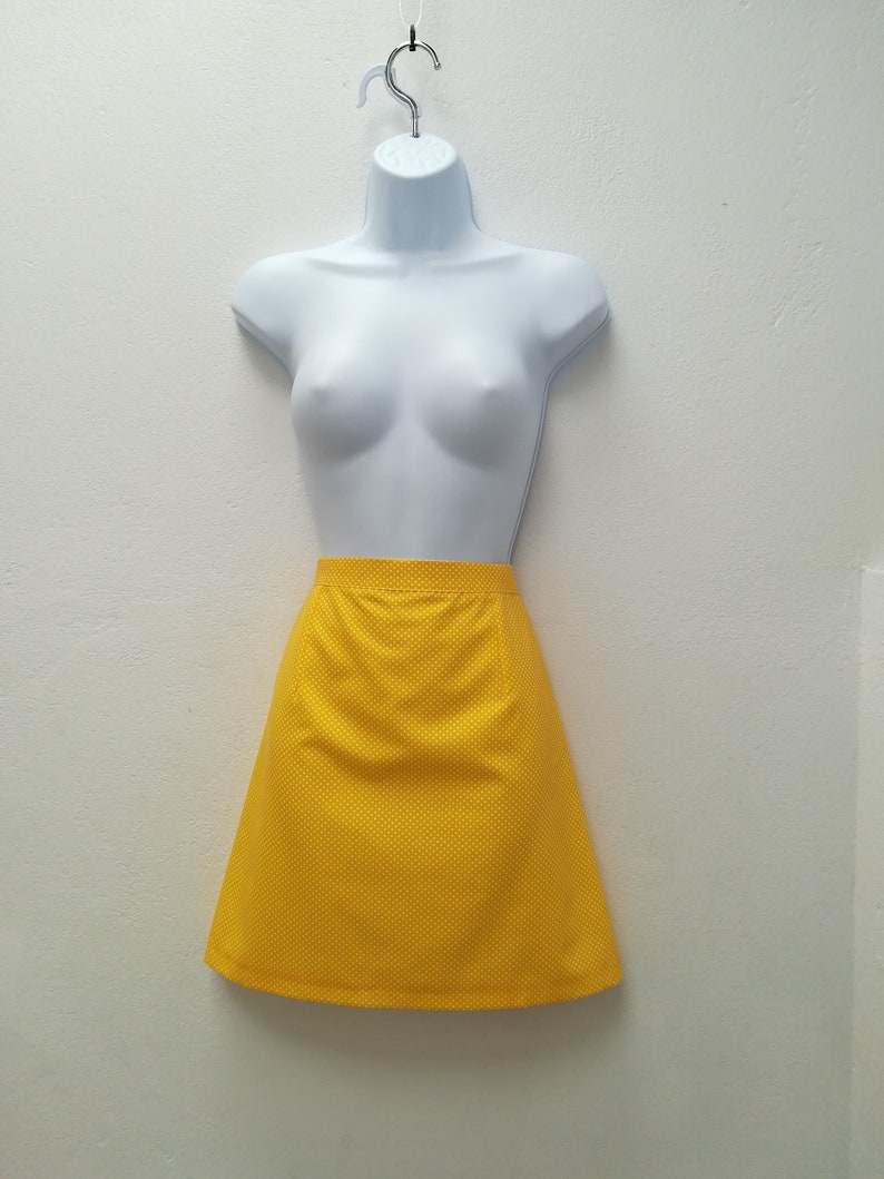 May include: A yellow mini skirt with a polka dot pattern. The skirt is made of a textured fabric and has a straight silhouette.
