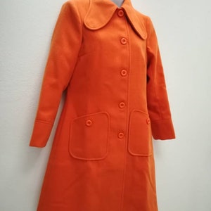 May include: A long, orange coat with a large collar and button closure. The coat has two large pockets on the front.