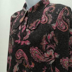 May include: A black long-sleeved shirt with a paisley pattern in pink, brown, and white. The shirt has a collared neckline and a sparkly texture.