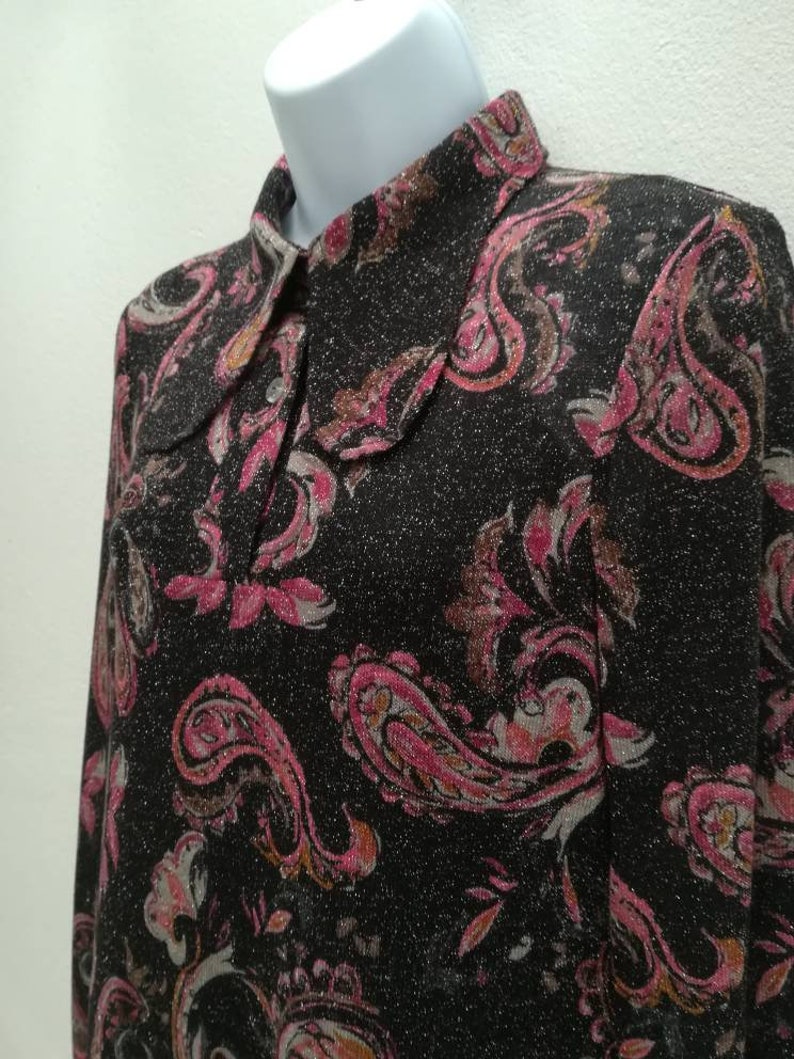 May include: A black long-sleeved shirt with a paisley pattern in pink, brown, and white. The shirt has a collared neckline and a sparkly texture.
