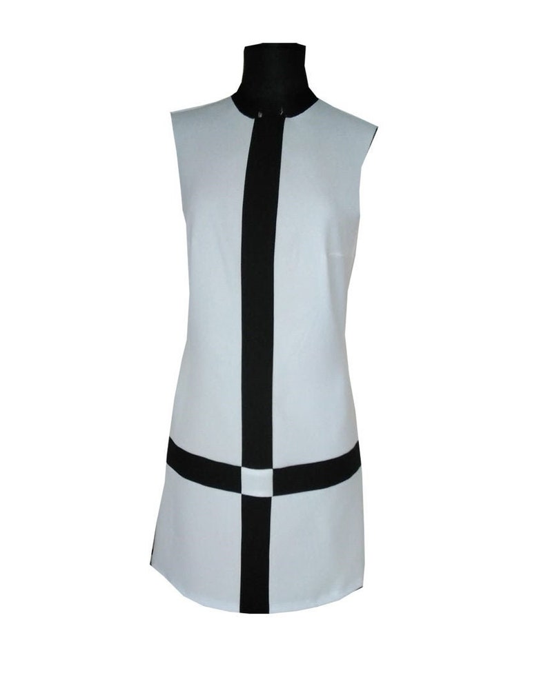 May include: A sleeveless white dress with a black vertical stripe down the center and a black horizontal stripe across the bottom. The dress has a mock neck.
