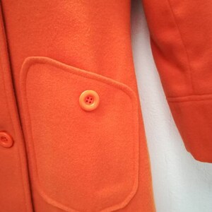 May include: A bright orange coat with a large patch pocket on the front. The pocket has a single button closure.