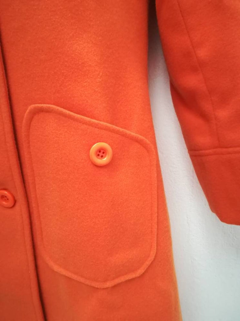 May include: A bright orange coat with a large patch pocket on the front. The pocket has a single button closure.