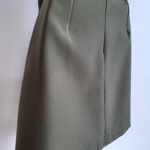 May include: Olive green skirt with a side zipper and a tailored design. The skirt has a classic, minimalist style, suitable for various occasions. The fabric appears to be a smooth, woven material. The skirt's length is approximately knee-length.