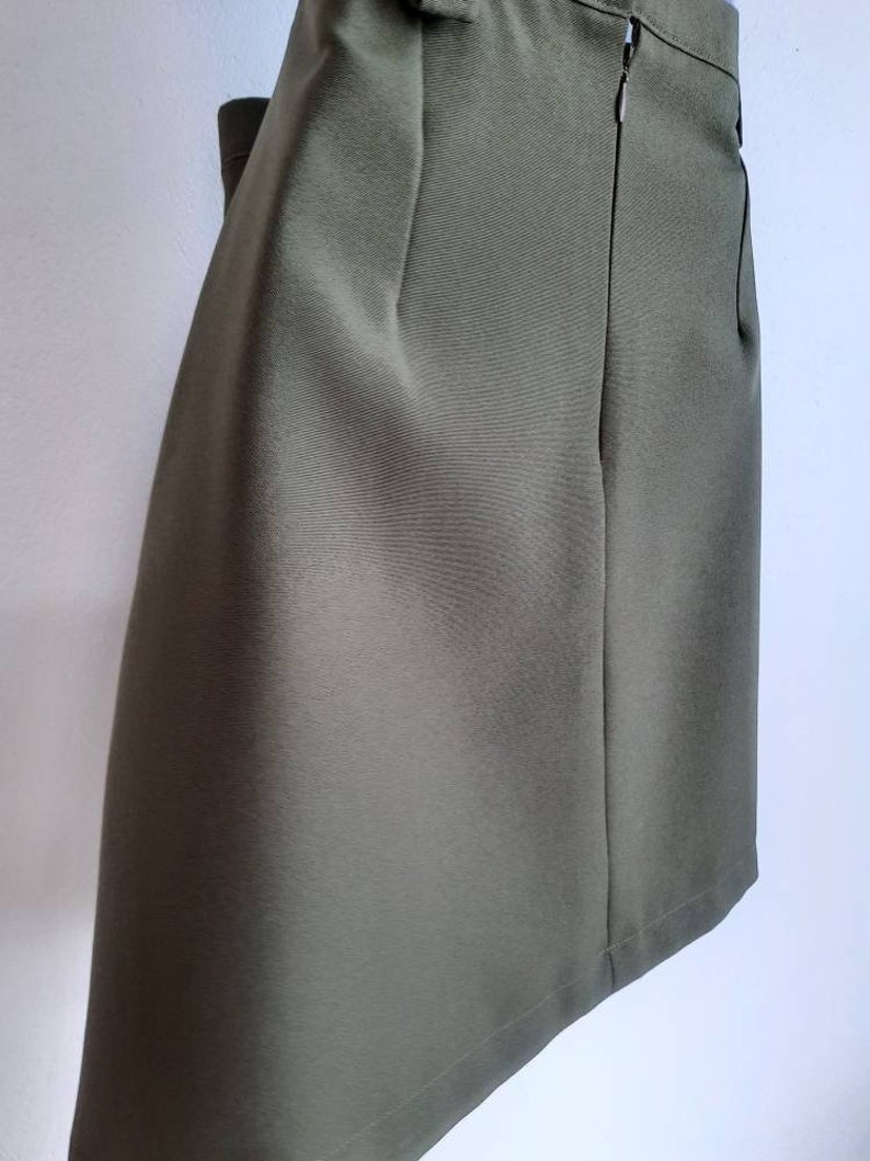 May include: Olive green skirt with a side zipper and a tailored design. The skirt has a classic, minimalist style, suitable for various occasions. The fabric appears to be a smooth, woven material. The skirt's length is approximately knee-length.