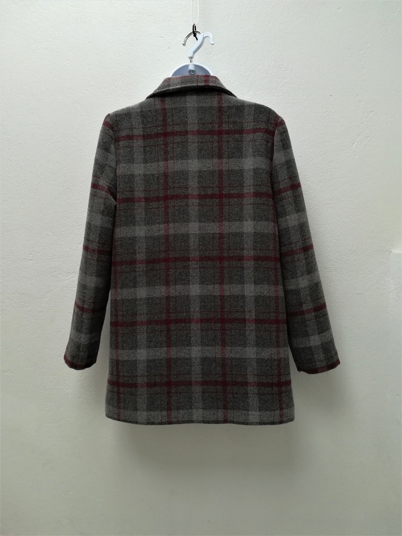 Puede incluir: Una chaqueta de traje gris y burdeos a cuadros con cuello de muesca y mangas largas.