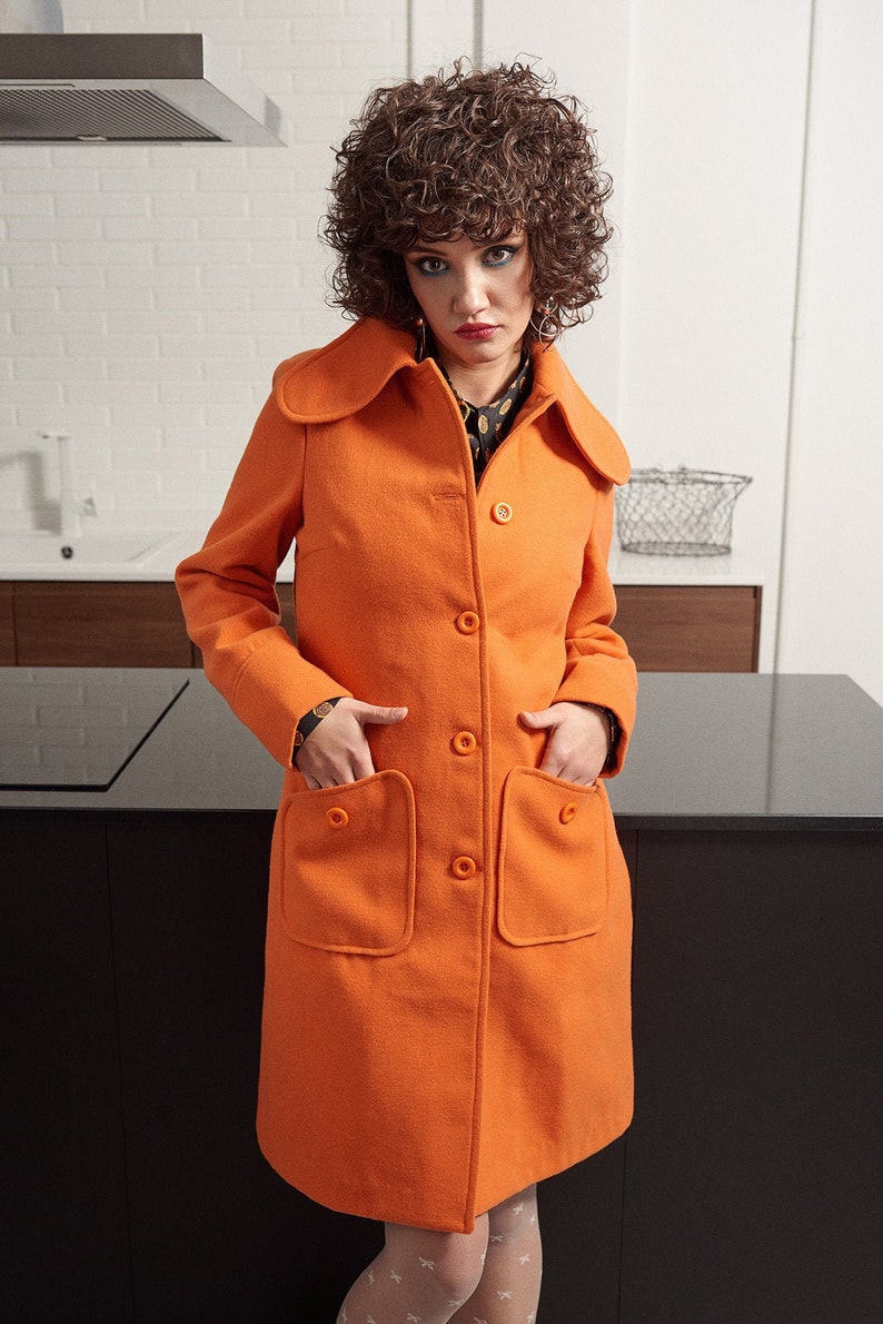 May include: A bright orange coat with a large collar and patch pockets. The coat has a button closure and is made of a soft, textured fabric.