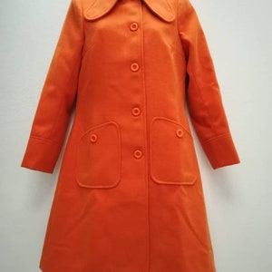 May include: A long-sleeved orange coat with a large collar and a button closure. The coat has two large pockets on the front.