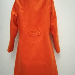 May include: A long, bright orange coat with a collar and two buttons on the back.
