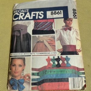 May include: A McCall's Crafts pattern envelope, featuring illustrations of belts, cummerbunds, and ties. The envelope has a blue and white header with the number 8861. The image shows various colors of the accessories, including red, blue, and black.