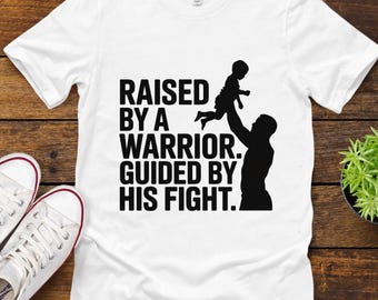 May include: White t-shirt with the text "RAISED BY A WARRIOR. GUIDED BY HIS FIGHT." in black. The graphic shows a silhouette of a person holding a child up in the air. White canvas sneakers with red trim are on the left.