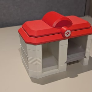 May include: A red and white storage box with a rounded top and a circular emblem. The box has a rectangular shape with open compartments. The design is reminiscent of a video game theme.