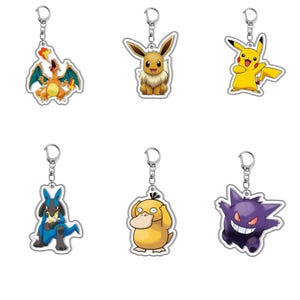 May include: A set of six acrylic keychains featuring various colourful cartoon creatures. The collection includes a fire-breathing orange dragon, a brown fox-like creature, a yellow electric mouse, a blue and black bipedal creature, a yellow duck, and a purple ghost.