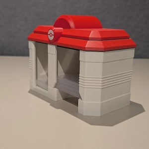 May include: A red and white, 3D-printed card holder, featuring a red roof with a white and red emblem. The card holder has a rectangular shape with a white base and a slot for cards. The design is reminiscent of a building.