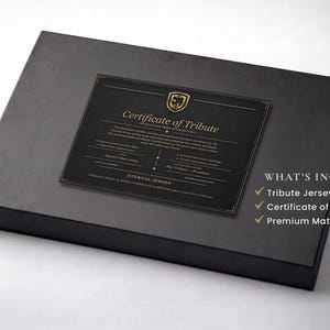 Pu&ograve; includere: Una confezione regalo nera con un certificato di tributo sopra. Il certificato ha scritte dorate e un logo dorato. Il testo "Eternal Jersey" &egrave; visibile. La confezione include una maglia tributo, un certificato e una confezione regalo nera opaca premium.