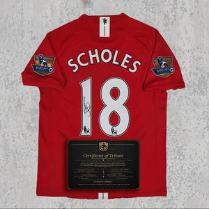 May include: Red jersey with the name "SCHOLES" and the number "18" in white. Features two Barclays Premier League patches and a "Certificate of Tribute" document. The jersey has a signature on the number 18.