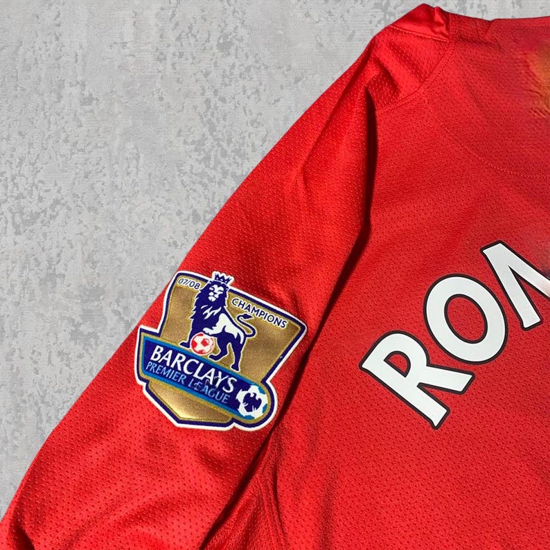 Pu&ograve; includere: Maglia da calcio rossa con la scritta "ROA" in bianco. La manica presenta una toppa Barclays Premier League Champions con un leone e la scritta "07/08". La maglia &egrave; realizzata in tessuto traspirante e strutturato.