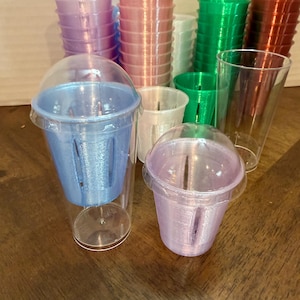May include: A collection of clear plastic cups with dome lids, each containing a colorful 3D-printed insert. The inserts come in various colors including blue, purple, green, red, and white, and feature vertical slots along the sides.