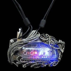 May include: A silver wire-wrapped pendant with a clear glass case containing a digital clock with red and blue LEDs. The pendant is attached to a black cord.