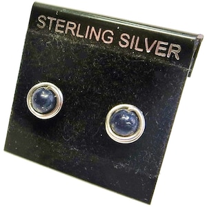 May include: A pair of sterling silver earrings with dark blue gemstone accents. The earrings are displayed on a black card with the words "Sterling Silver" printed on it.