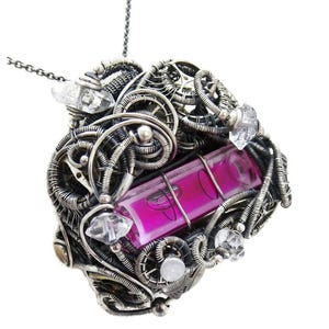 May include: A handcrafted silver pendant necklace featuring a complex wire-wrapped design. The pendant incorporates a rectangular, magenta-colored stone and is accented with clear crystal and white stone embellishments. The necklace has a delicate silver chain.