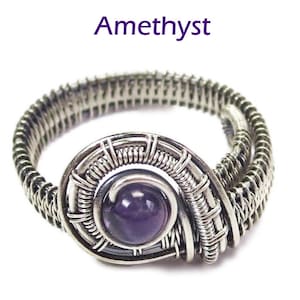 May include: A silver wire wrapped ring with a purple amethyst gemstone. The ring is made with a woven wire design.