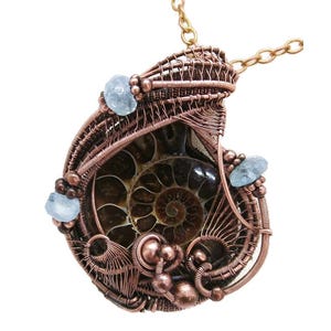 May include: A copper wire wrapped pendant featuring a fossilized ammonite with a swirling pattern. The pendant is accented with light blue aquamarine stones.