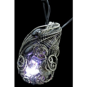 May include: A silver wire-wrapped pendant with black gemstones and a clear, glowing light source in the center. The pendant is shaped like a teardrop and has a delicate, intricate design.
