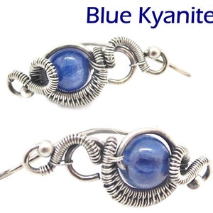 May include: A pair of earrings featuring a blue kyanite gemstone. The gemstones are encased in a silver-colored wire wrap design. The text "Blue Kyanite" is displayed above the earrings.