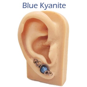 May include: A blue kyanite gemstone earring with copper wire wrapping. The earring is shown on a model ear.