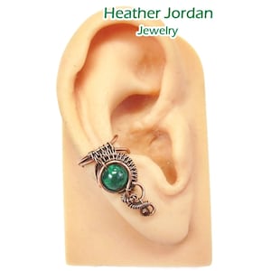 May include: A copper wire ear cuff with a green malachite stone. The cuff is designed to wrap around the upper part of the ear.