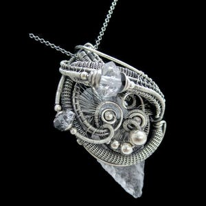 May include: Silver wire wrapped pendant featuring a clear quartz crystal and a smaller black crystal. The pendant is attached to a silver chain.
