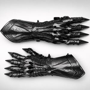 May include: A pair of black articulated gauntlets featuring intricate embossed scrollwork patterns on the forearm plates, segmented finger coverings, and sharp, pointed metal tips extending from each fingertip, crafted with a polished finish.