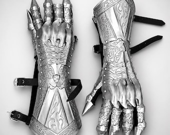 May include: A pair of silver-colored metal gauntlets featuring articulated finger plates with pointed tips, intricate embossed scrollwork patterns, and black leather straps with metal buckles for secure fastening around the wrist and forearm.