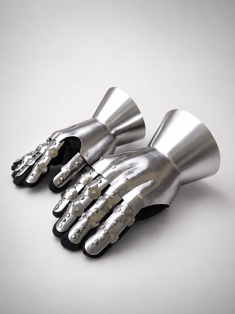May include: A pair of articulated metal gauntlets featuring a polished silver finish. Each gauntlet consists of a flared cuff, a protective plate for the back of the hand, and segmented finger coverings secured with small rivets over a black lining.
