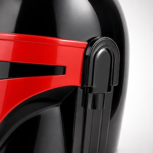 May include: A glossy black helmet featuring a prominent, horizontal red visor section across the front. The helmet has a smooth, rounded dome and a distinct vertical side panel detail integrated into the design, creating a bold contrast.