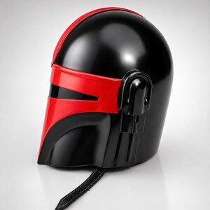 May include: A glossy black and red helmet featuring a T-shaped visor opening, a smooth rounded dome, and a side-mounted ear piece. A black leather-like chin strap with visible stitching hangs from the bottom edge of the helmet structure.