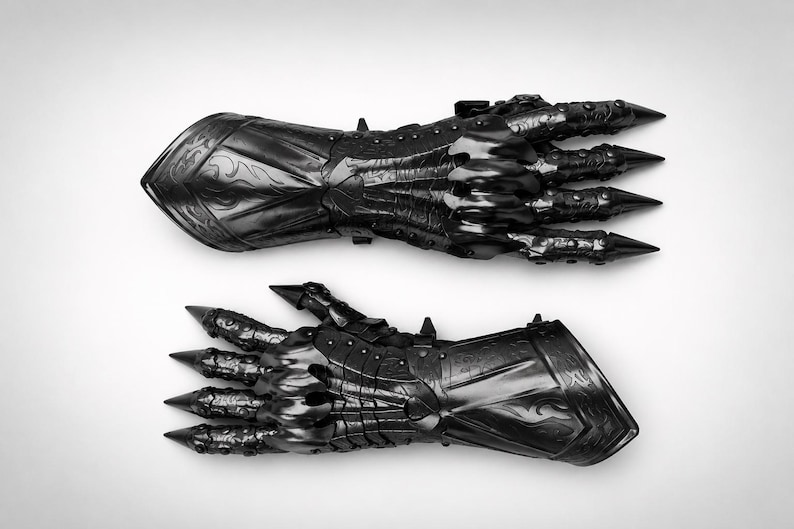 May include: A pair of black articulated gauntlets featuring intricate embossed scrollwork patterns on the forearm plates, segmented finger coverings, and sharp, pointed metal tips extending from each fingertip, crafted with a polished finish.