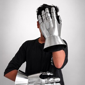 May include: A pair of polished steel gauntlets featuring articulated finger plates, riveted construction, and flared cuffs. These metallic hand protectors are designed with segmented sections for the fingers and thumb, providing a reflective surface.