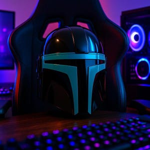 May include: A glossy black helmet featuring a distinct T-shaped visor design with bright cyan blue accents along the faceplate. The helmet has a smooth, reflective surface and a structured, rounded top, presented in a dark, gaming-themed environment.