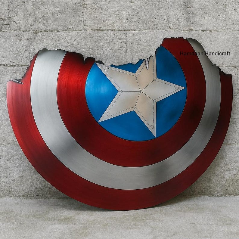 May include: A distressed Captain America shield with a star in the center. The shield is red, white, and blue, with a silver-colored outer ring. The shield has a battle-worn appearance with a jagged edge.