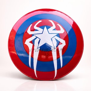 May include: A round shield with a red, white, and blue color scheme. The shield has a white star in the center, with white stylized wing-like shapes. The text "VALOR FORGE CRAFTS" is visible on the shield.