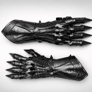 May include: A pair of black articulated gauntlets featuring intricate embossed scrollwork patterns on the forearm plates, segmented finger coverings, and sharp, pointed metal tips extending from each fingertip, crafted with a polished finish.