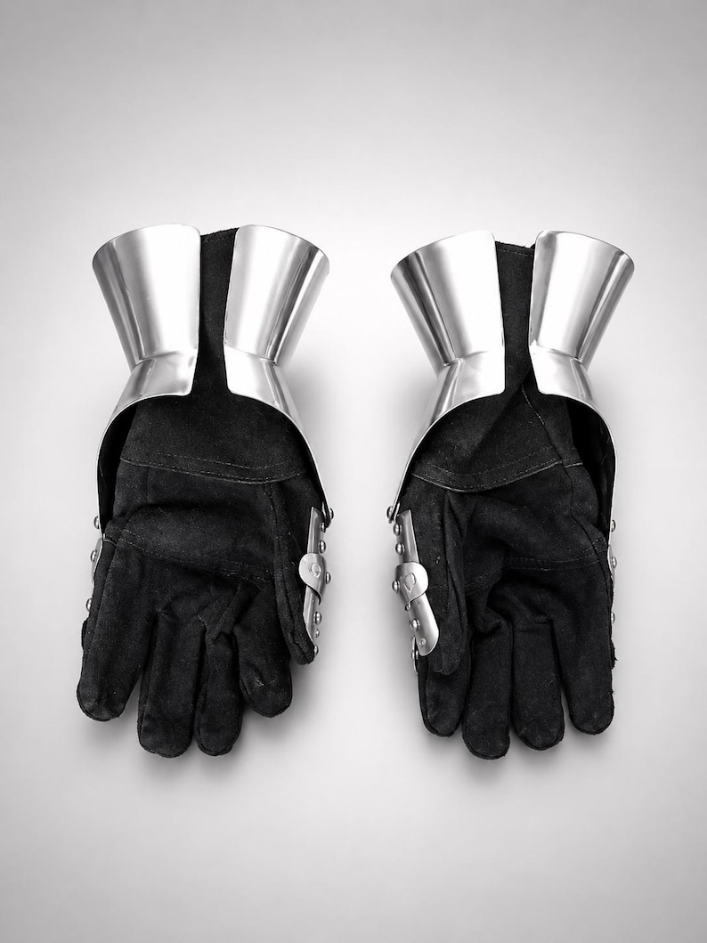May include: A pair of black gloves featuring polished silver metal gauntlet cuffs and articulated metal plates along the outer edges. The gloves are constructed from a dark, textured fabric and include visible rivets securing the metal components.