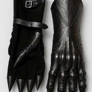 May include: A pair of black gauntlets featuring articulated finger plates with pointed tips, embossed scrollwork patterns on the hand and wrist sections, and adjustable leather straps with metal buckles at the forearm for a secure fit.