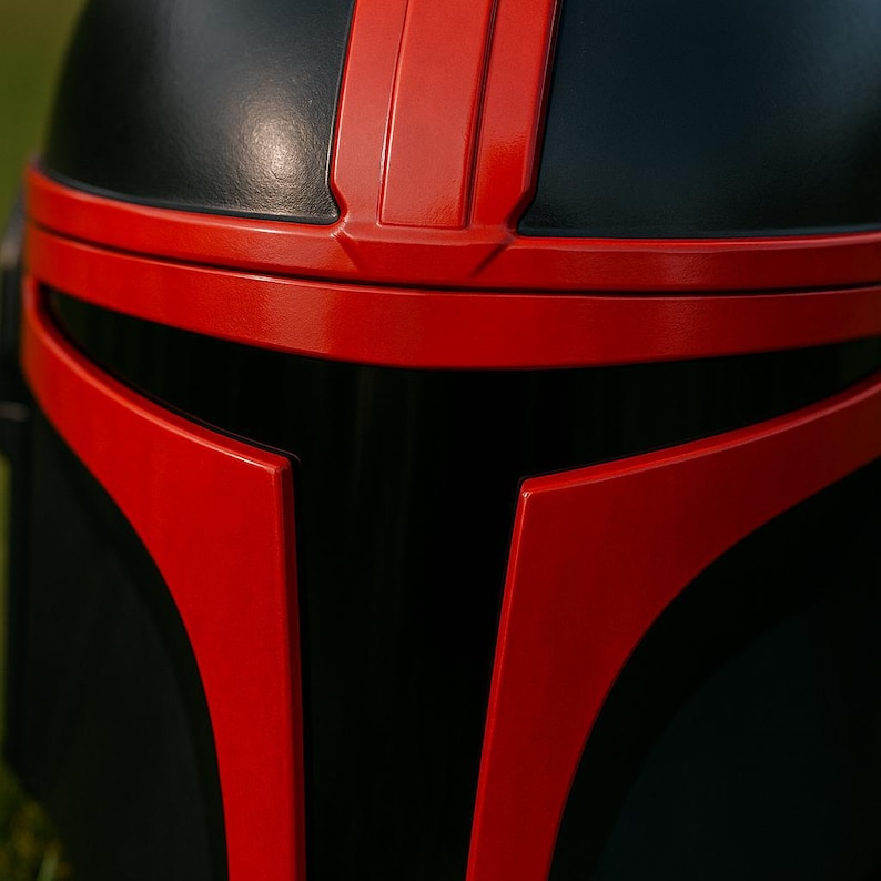 May include: A full-face helmet featuring a matte black finish with glossy red accents. The design includes a prominent red T-shaped visor frame and a vertical red stripe running along the center of the dome, creating a bold contrast.