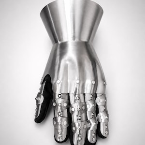 May include: A metallic gauntlet featuring a flared cuff and articulated finger plates. The armor is constructed from polished steel segments secured with rivets over a black fabric base, covering the hand and wrist with a protective structure.