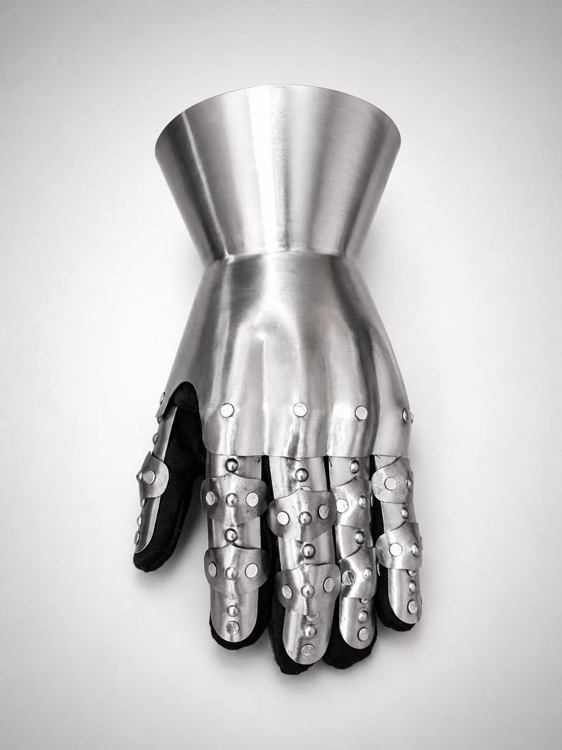 May include: A metallic gauntlet featuring a flared cuff and articulated finger plates. The armor is constructed from polished steel segments secured with rivets over a black fabric base, covering the hand and wrist with a protective structure.